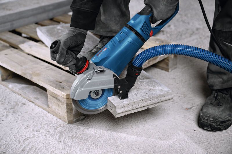 A person wearing safety equipment cuts a concrete slab with a large angle grinder.