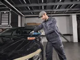 A person wearing safety equipment polishes a car hood with a power tool.
