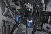 A person wearing safety equipment uses an impact wrench to tighten bolts on machinery.