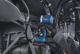 A person wearing safety equipment uses a cordless impact wrench on industrial machinery.