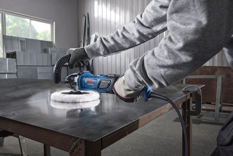 Person wearing safety equipment using a polisher on a metal workbench.