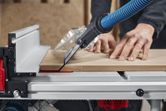 A person pushes wood through a table saw with dust extraction in a workshop.