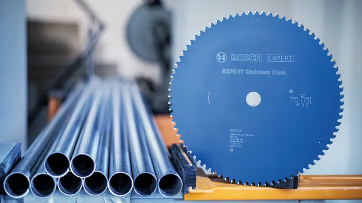 Circular saw blade next to stacked metal pipes on an industrial workstation.