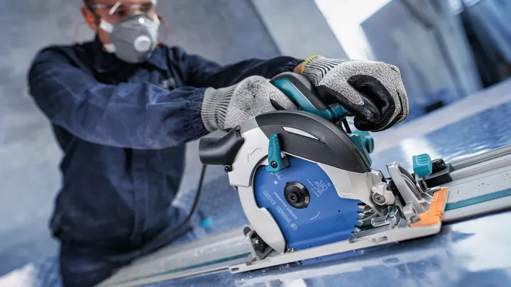 Person wearing safety equipment operates a circular saw to cut a metal sheet.
