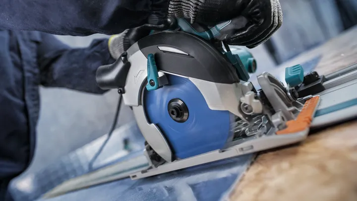 Person wearing safety equipment uses a circular saw to cut wood along a guide rail.