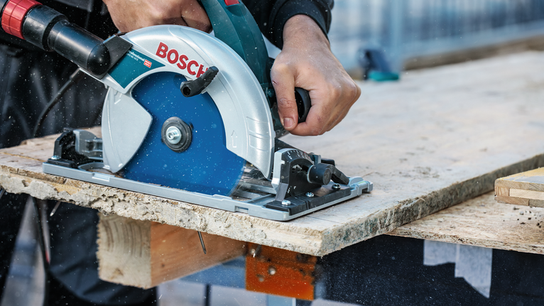 Person operating a circular saw to cut a wooden board on a workbench.