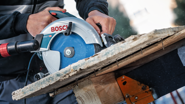 Person operating a circular saw to cut wood outdoors.