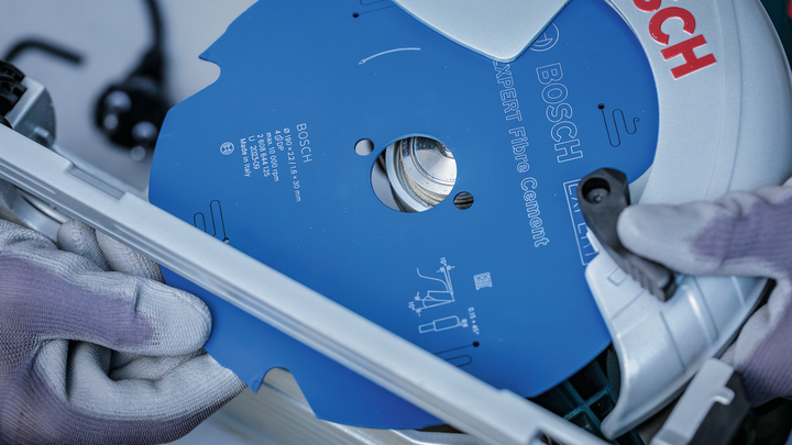 Person wearing safety equipment installs a blue circular saw blade into a power tool.