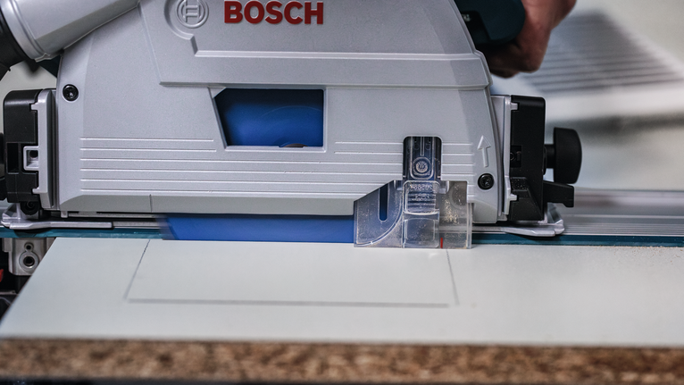 Person operating a circular saw to cut a panel along a straight guide.
