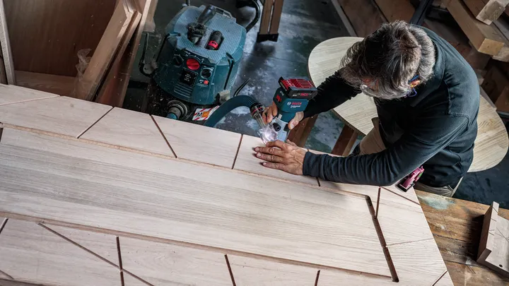 Person cutting geometric patterns into wood with a power tool in a workshop.
