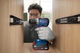 A person wearing safety equipment uses a cordless drill driver to assemble a wooden cabinet.