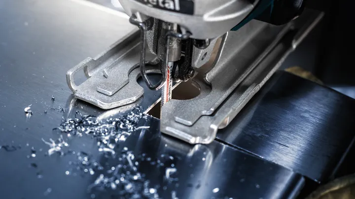Jigsaw cutting a sheet of metal, small metal shavings scattered around the blade.