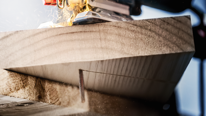 Jigsaw cutting through thick wooden plank with sawdust scattering.