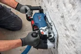 A person wearing safety equipment uses a wall chaser to cut a groove into plaster.
