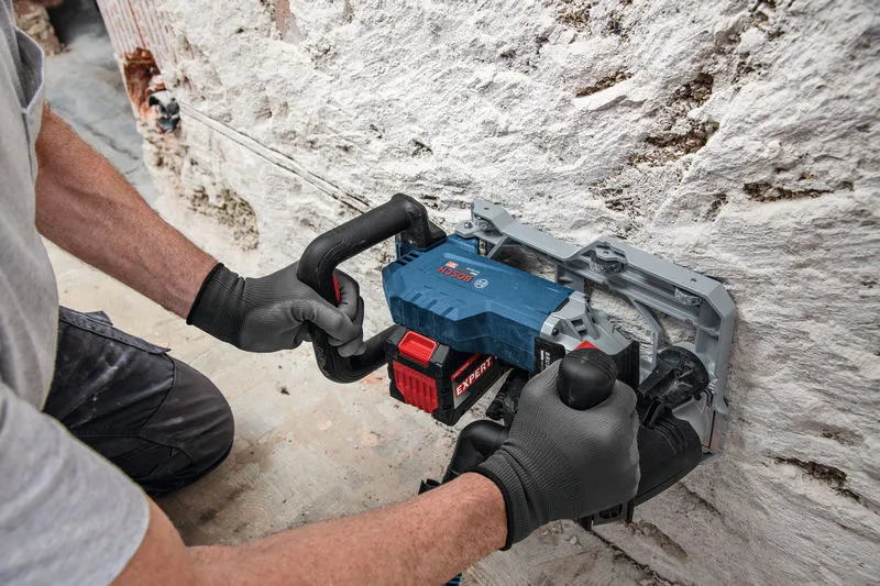 Person wearing safety equipment operates a wall chaser to cut a groove in a masonry wall.