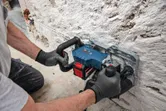 Person wearing safety equipment operates a wall chaser to cut a groove in a masonry wall.
