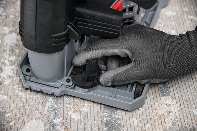 Person wearing safety equipment adjusts a wall chaser depth dial on a concrete floor.