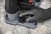 Person wearing safety equipment adjusts a wall chaser depth dial on a concrete floor.