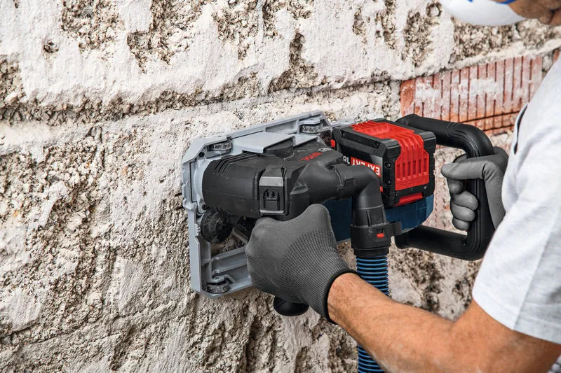 A person wearing safety equipment uses a wall chaser to cut grooves in a concrete wall.