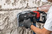 A person wearing safety equipment uses a wall chaser to cut grooves in a concrete wall.
