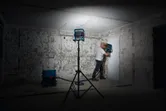 A person wearing safety equipment operates a wall drilling tool under work light.