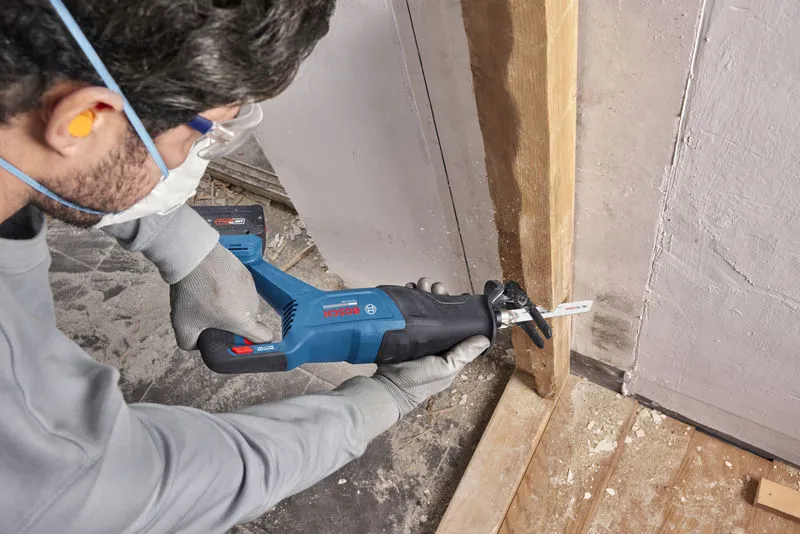 A person wearing safety equipment cuts a wooden beam with a cordless reciprocating saw.