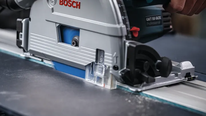 Person wearing safety equipment guides a circular saw along a straight metal rail.