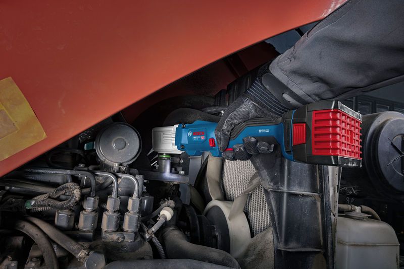 A person wearing safety equipment uses a cordless impact wrench on an engine.