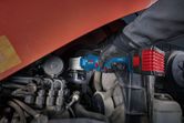 A person wearing safety equipment uses a cordless impact wrench on an engine.