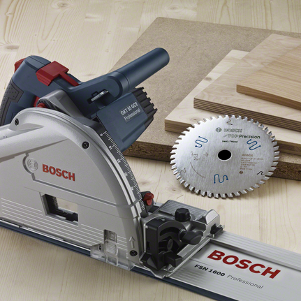 Track saw with a circular blade next to stacked wood boards on a workbench.